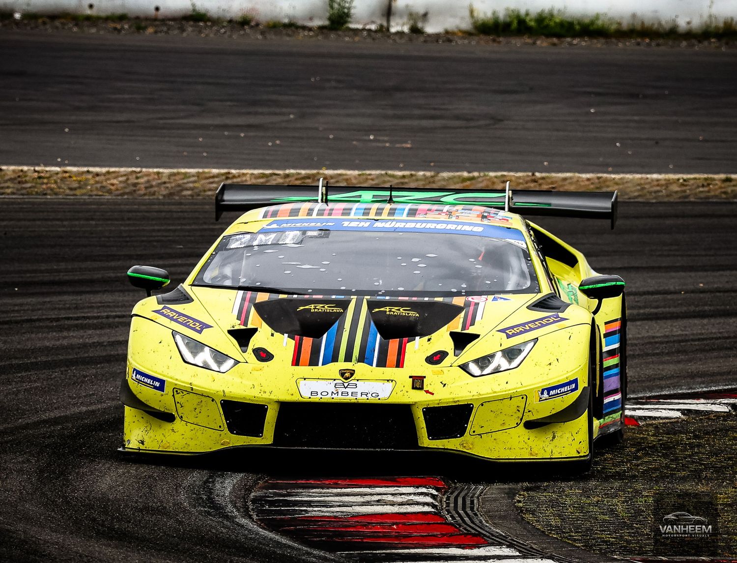 Yellow Lamborghini Huracan GT3 race car with colorful livery navigating a track corner during a motorsport competition.