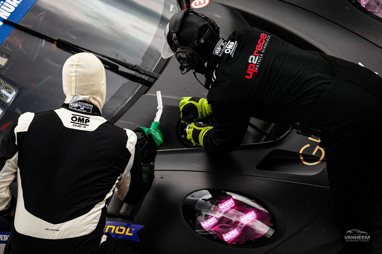 Two race car mechanics in OMP gear work on a black racing car with UP2TECH livery in pit lane.