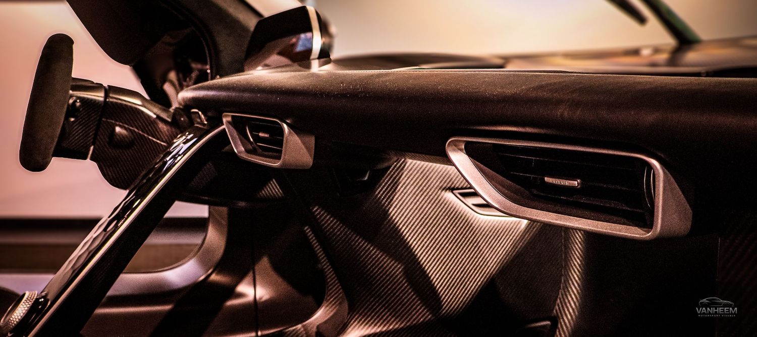 Luxury car interior featuring carbon fiber dashboard trim, sleek air vents, and premium leather upholstery in warm lighting.