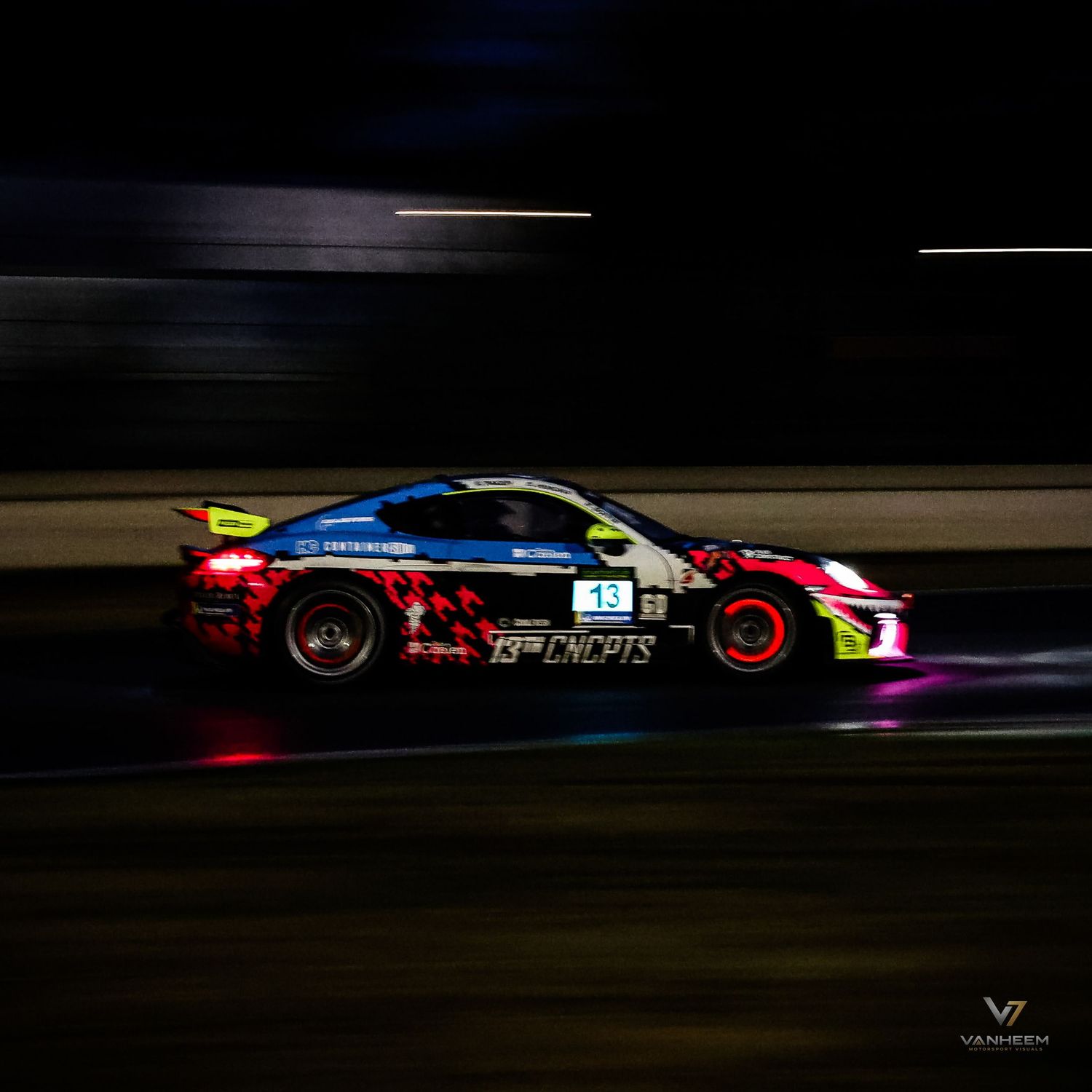 A colorful race car speeds around a track at night, captured with motion blur in dramatic lighting.