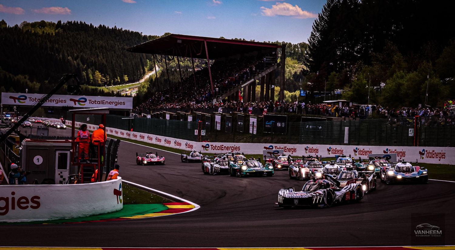 Racing cars compete at the start of a Le Mans endurance race at Spa-Francorchamps circuit at dusk.