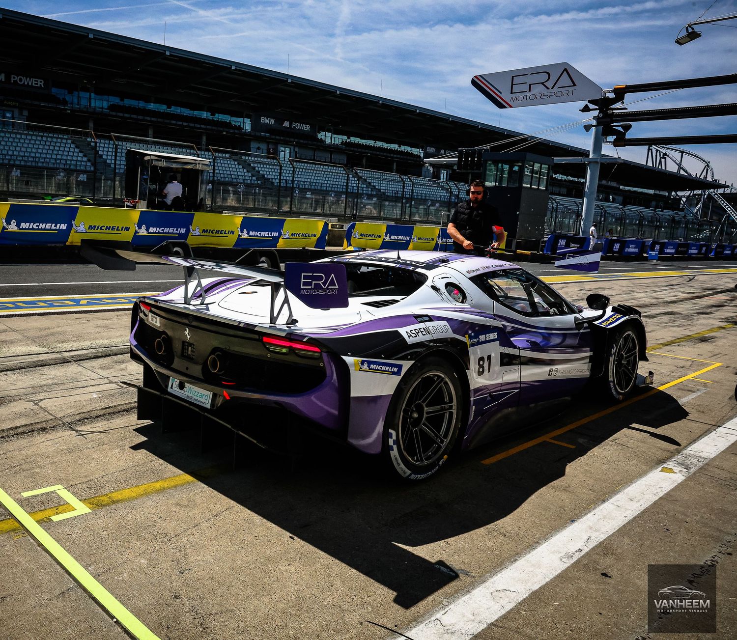 Purple ERA racing car parked in pit lane at a motorsport circuit during a sunny race event.