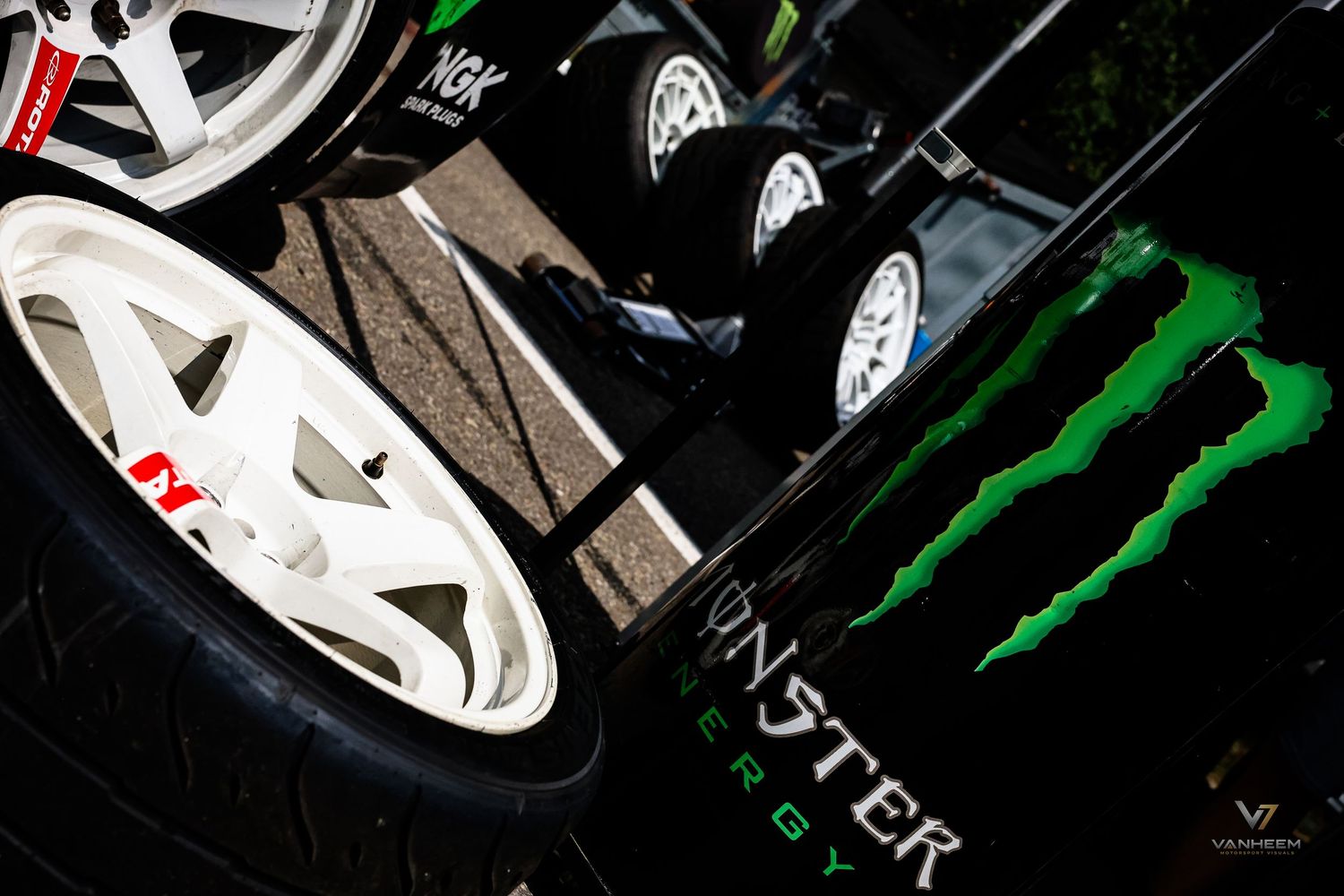 Monster Energy racing car with white alloy wheels and performance tires displayed at a motorsport event.