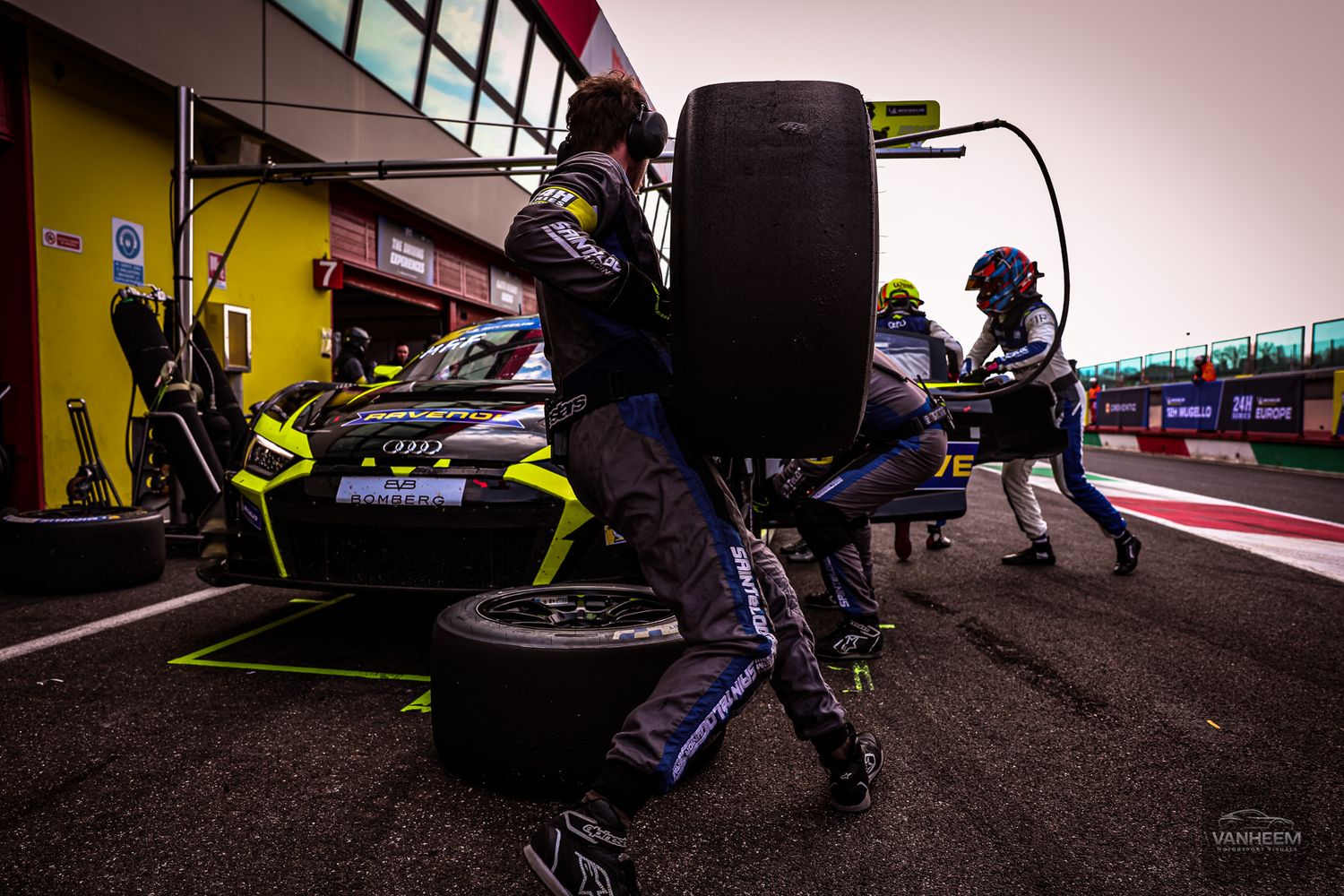 Racing pit crew members perform maintenance on a Formula 1 car during a pit stop at a racetrack.