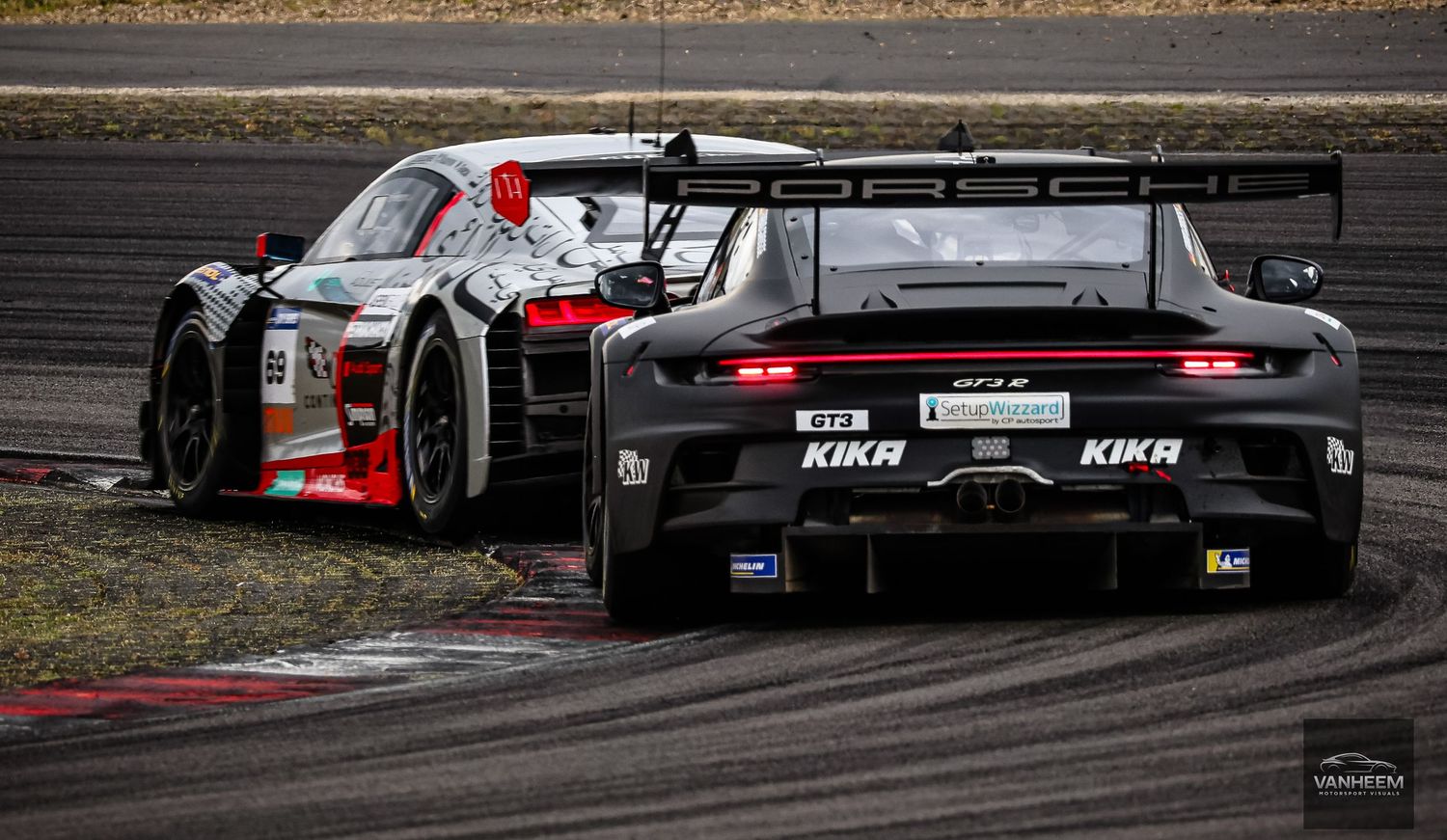 Black Porsche GT3 race car with KIKA sponsorship navigating a track corner during a motorsport competition.