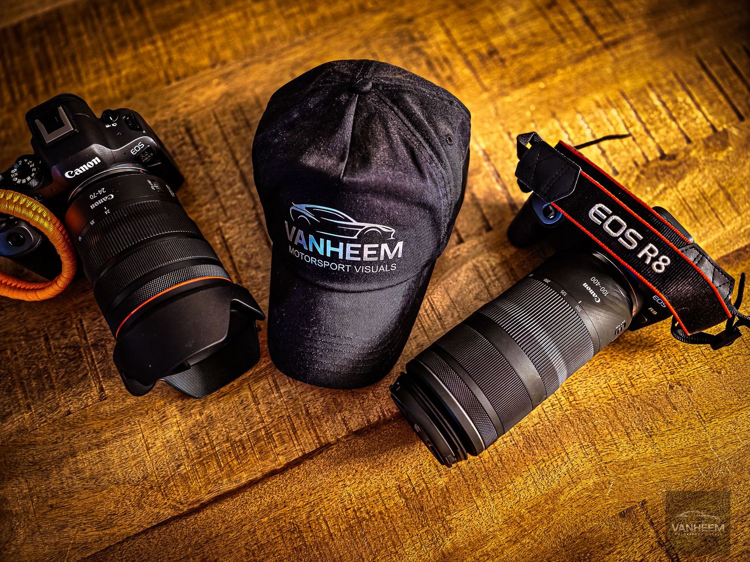 Two Canon cameras with lenses and a Vanheem branded cap arranged on a wooden surface.