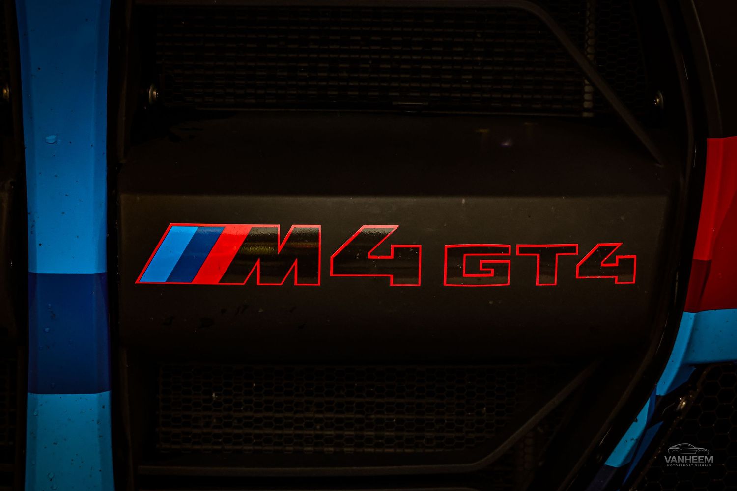 Close-up of BMW M4 GT4 emblem badge on a dark carbon fiber panel with blue and red accents.