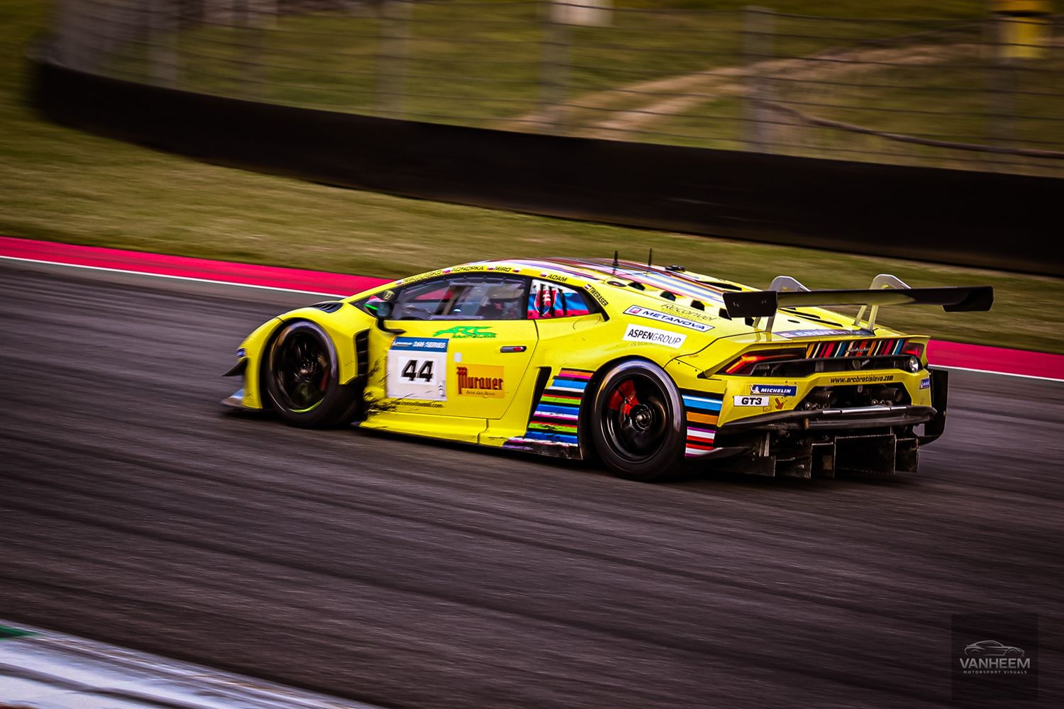 Yellow Lamborghini race car speeds around track corner during competitive motorsport event.