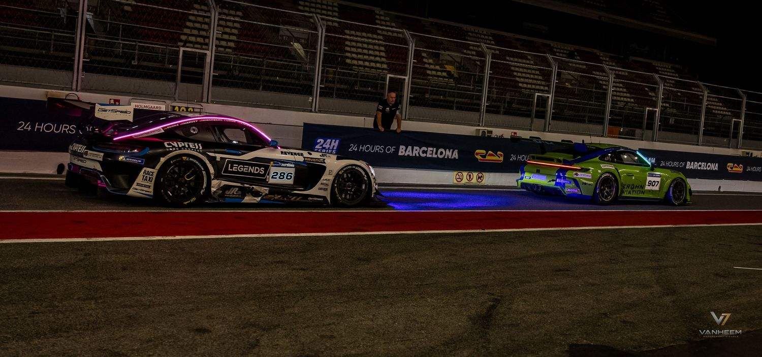 Two GT racing cars compete side by side on an illuminated night circuit during the 24 Hours of Barcelona endurance race.