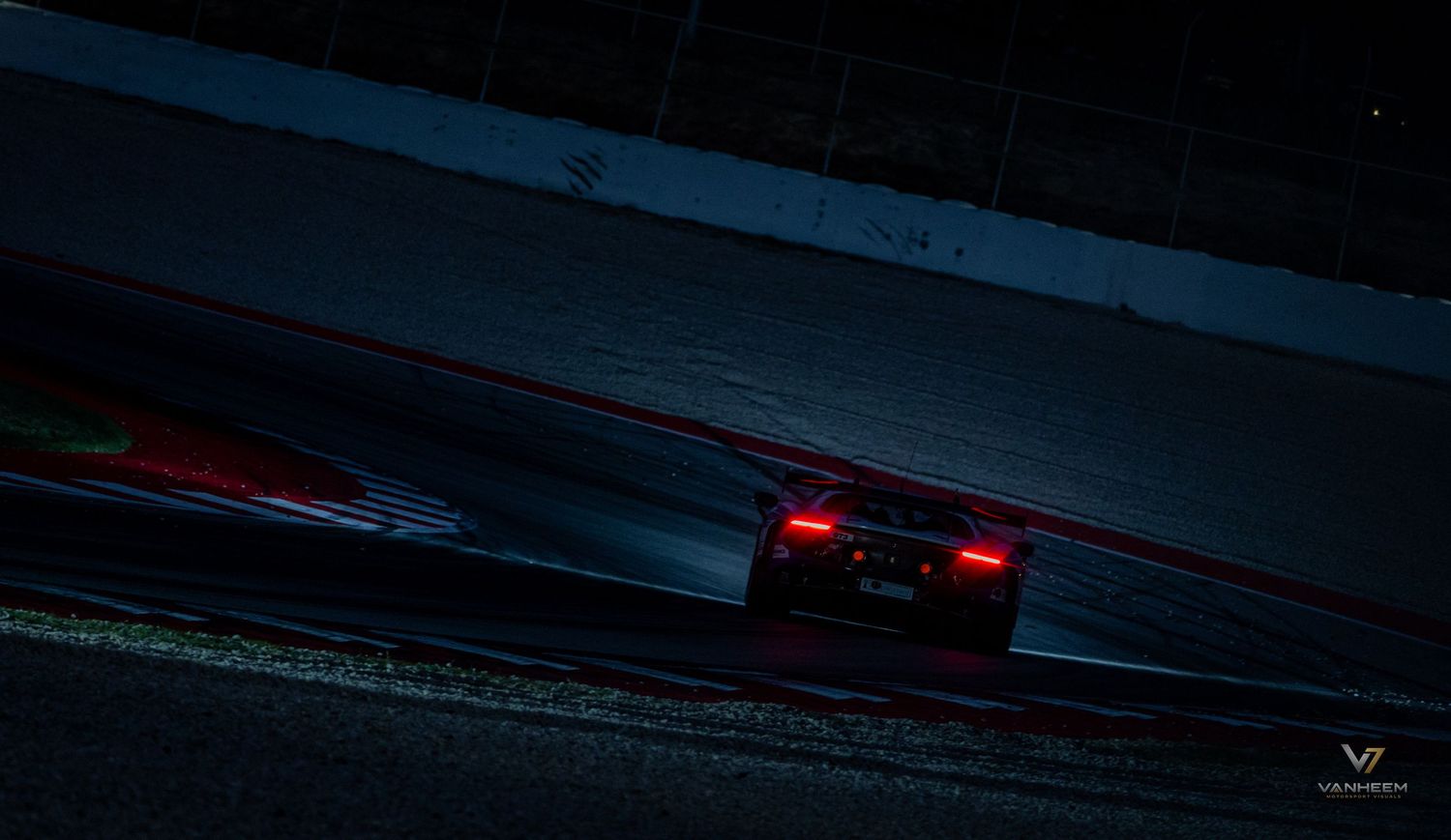A racing car speeds around a dark circuit track at night, illuminated by glowing red brake lights.