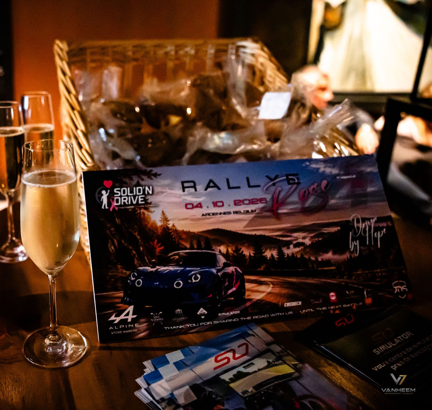Signed Rally5 event poster displayed on a table beside a champagne flute at an upscale venue.