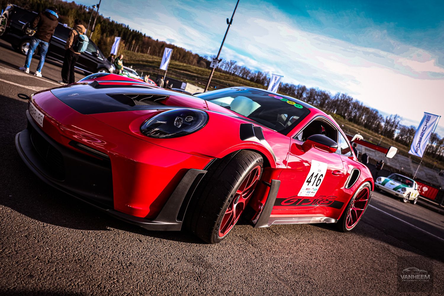 Red Porsche 911 GT3 race car with number 415 on track at motorsport event, featuring wide body kit and red wheels.