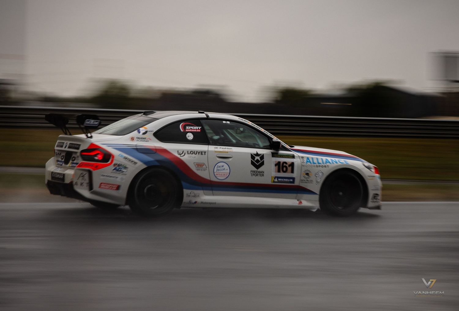 White BMW M2 race car number 161 with sponsor decals speeding on wet track during motorsport competition.