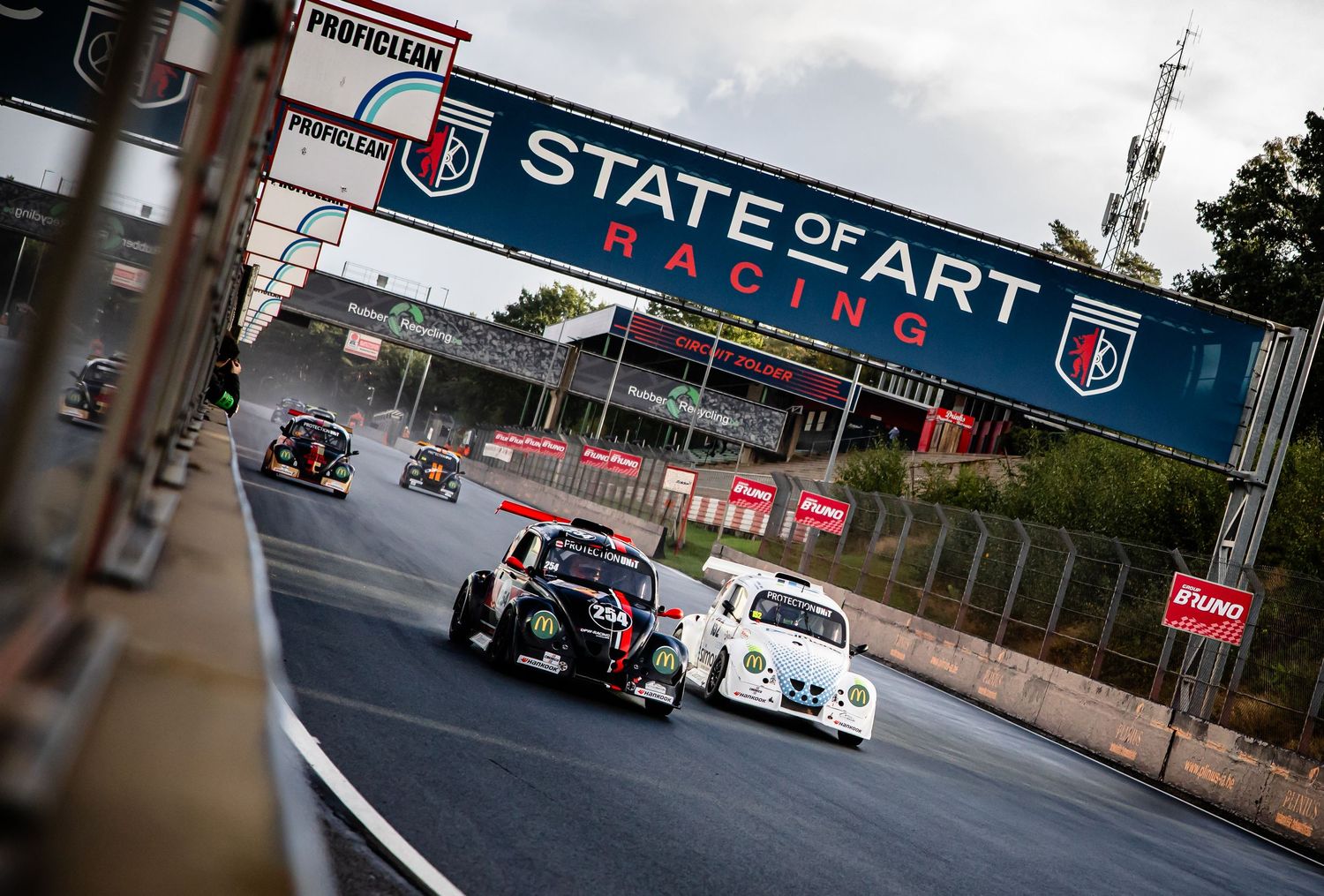 Racing cars compete on a circuit under a State of Art Racing banner during an exciting motorsport event.
