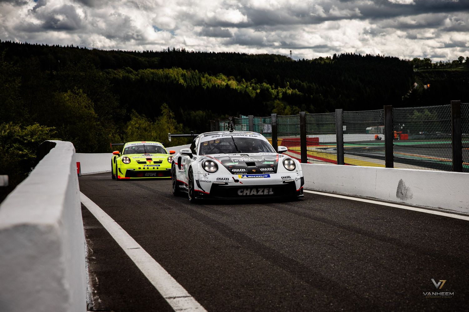 Porsche GT3 race cars competing on a wet circuit at Spa-Francorchamps during a cloudy motorsport event.