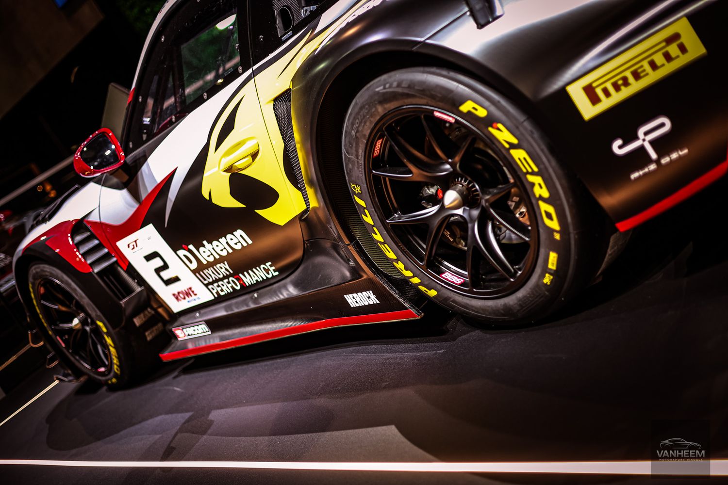 Racing cars with Pirelli tires showcased in dramatic low-key lighting at motorsport event.