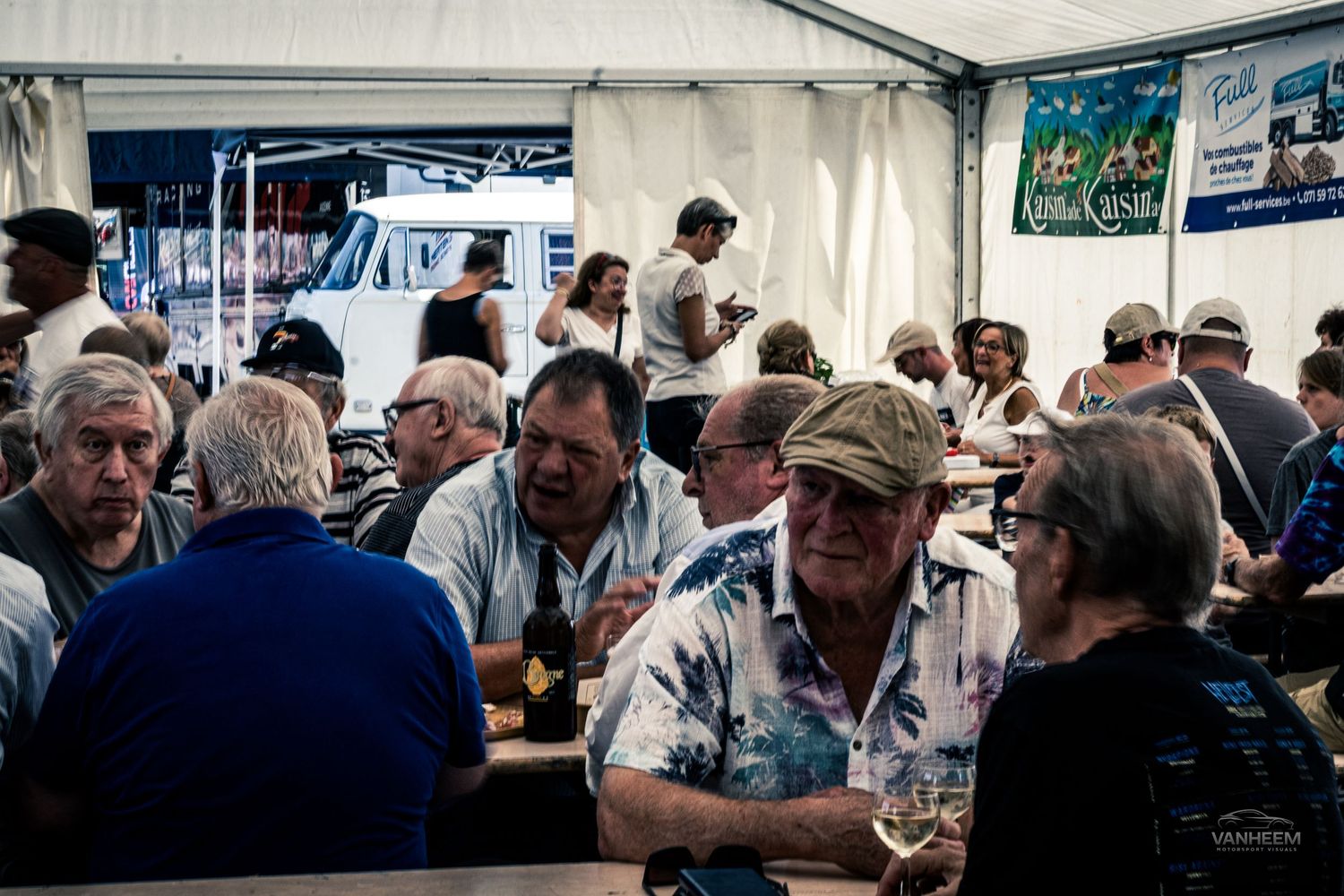 A crowded beer tent filled with people enjoying drinks and conversation at an outdoor festival event.