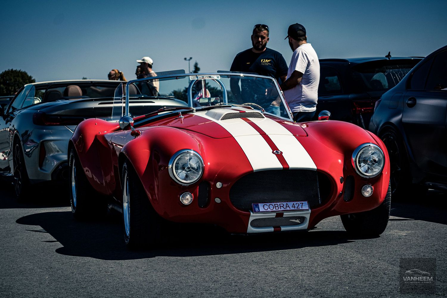 Classic red vintage race cars lined up at a motorsport event against a dark blue sky background.