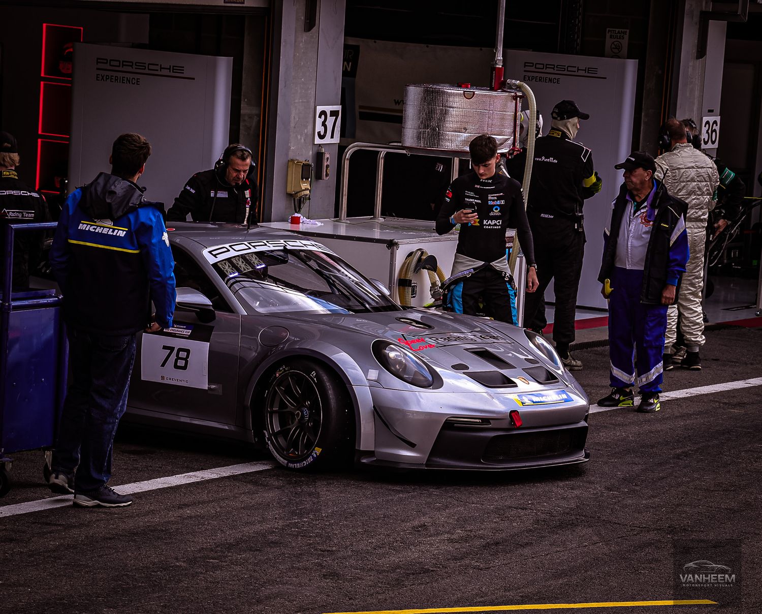 White racing cars parked in pit garage with crew members preparing for race.
