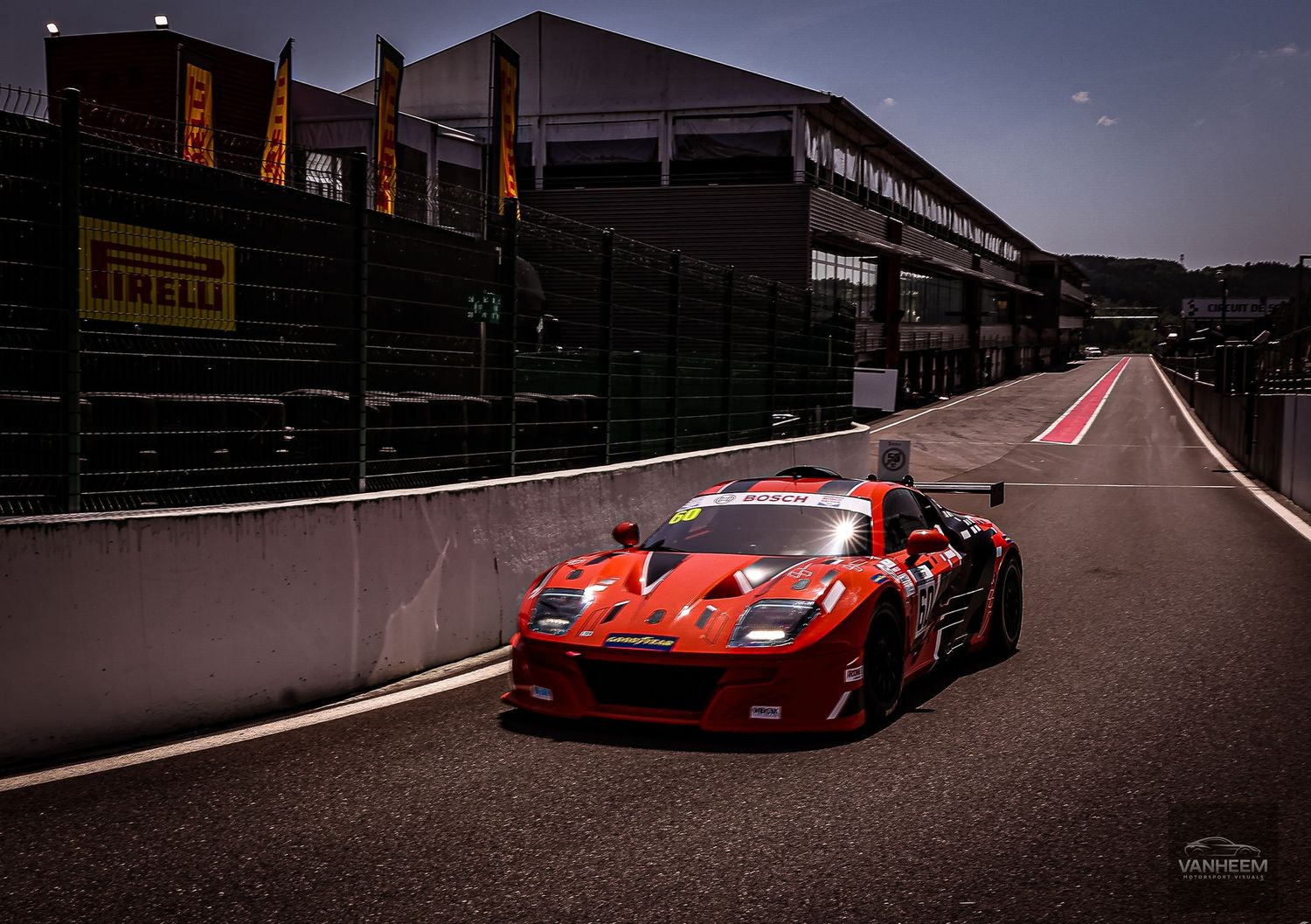 Red Ferrari GT3 racing car on pit lane at Spa-Francorchamps circuit with Pirelli advertising boards.