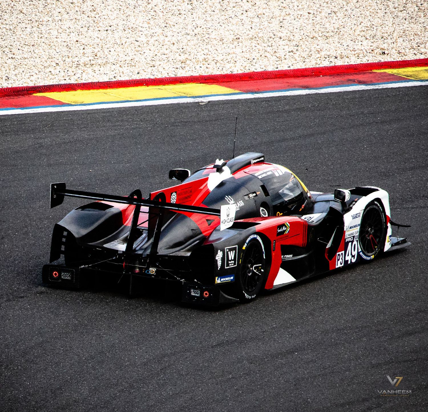 Red and black #49 LMP race car speeding on a circuit track during an endurance motorsport event.