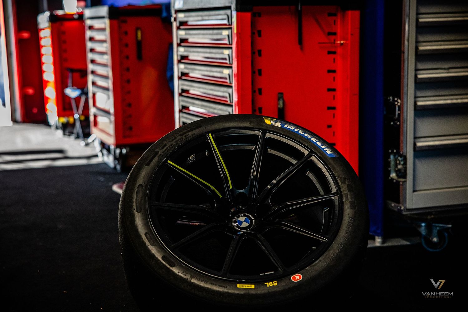 BMW black alloy wheel with racing tire in a motorsport garage with red tool chests in the background.
