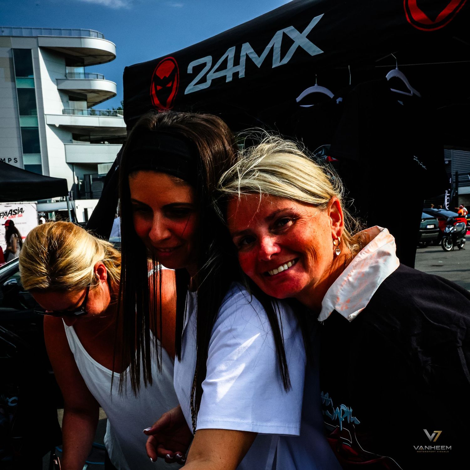 Two women smiling and posing together at a 24MX motorsport event outdoors on a sunny day.
