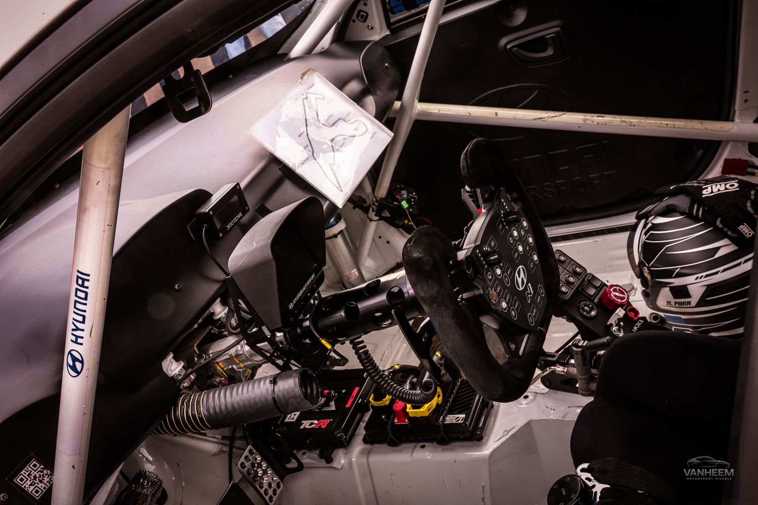 Interior of a Hyundai rally car cockpit featuring a racing steering wheel, roll cage, and complex wiring setup.