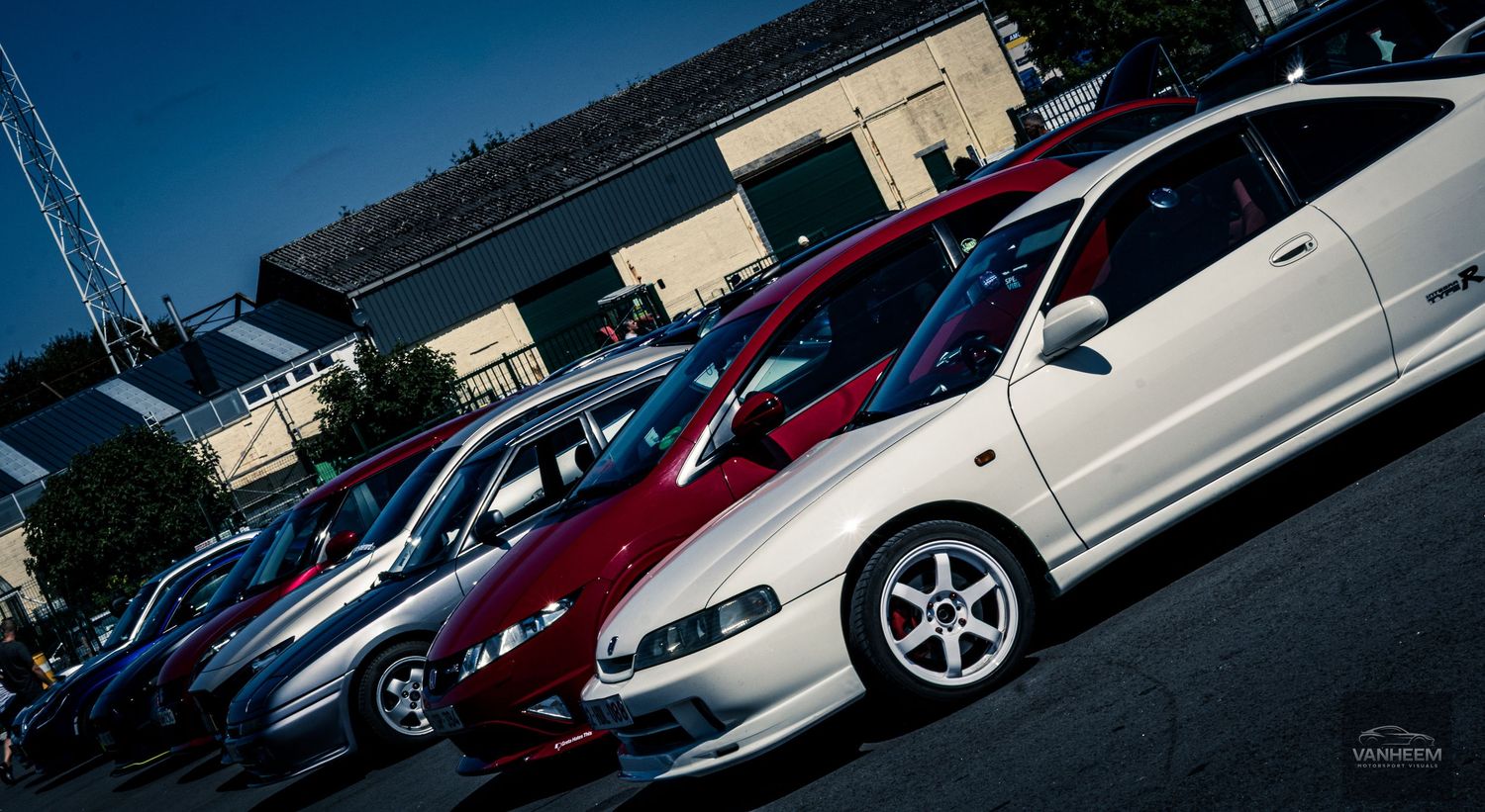 A row of parked cars including Subaru WRX and other performance vehicles in a parking lot during daytime.