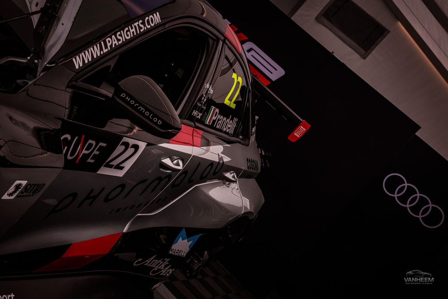 Dark racing car number 22 with Audi branding displayed at an indoor motorsport event under dramatic lighting.