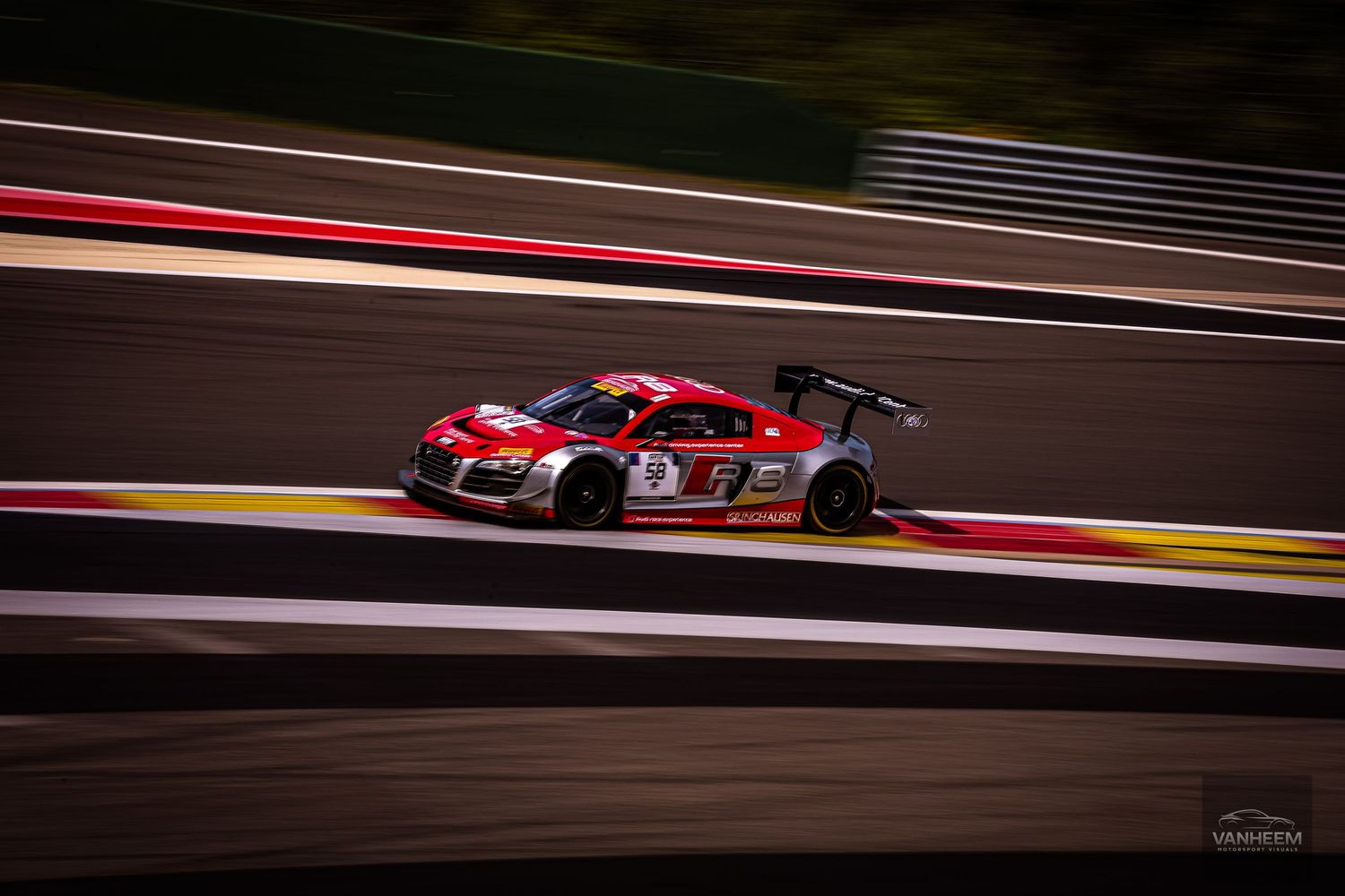 Red Audi racing car speeding on a circuit track during a motorsport endurance race event.