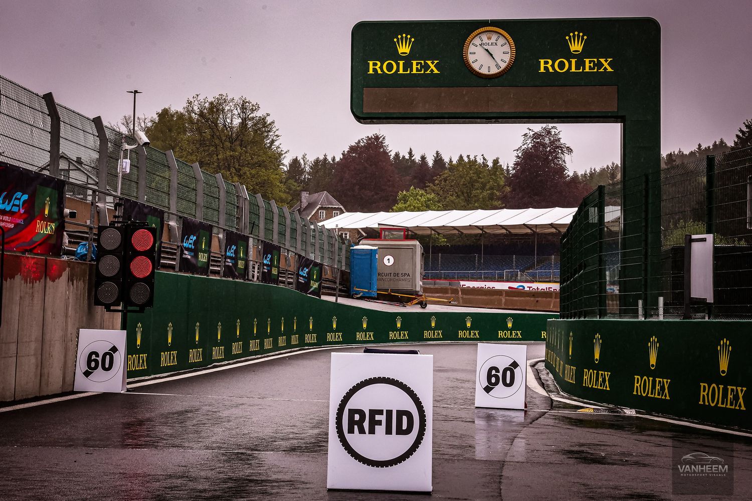 Rainy pit lane entrance at Spa-Francorchamps F1 circuit with Rolex clock arch and RFID checkpoint sign.