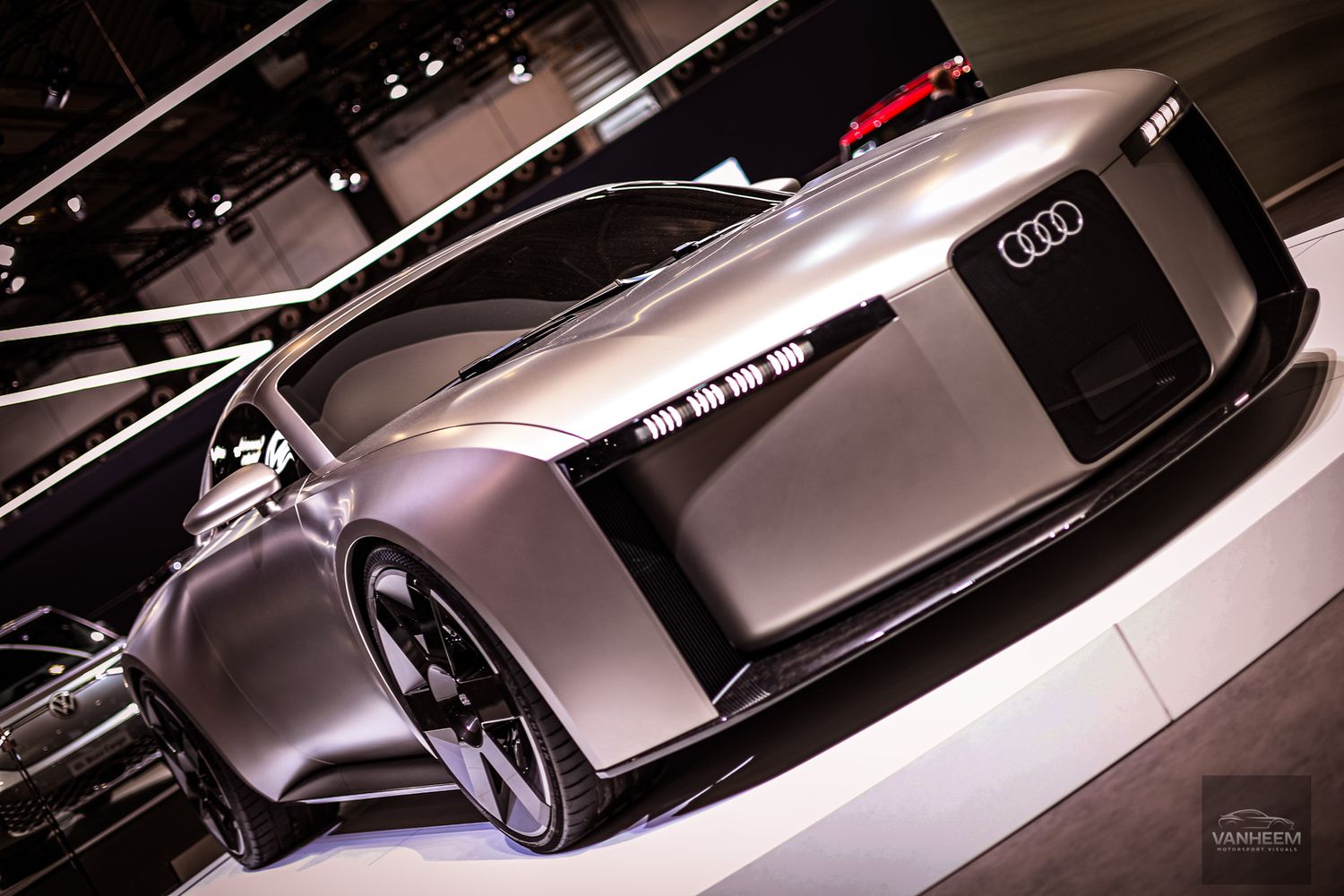 Luxury concept cars displayed in silver metallic finish under dramatic showroom lighting.