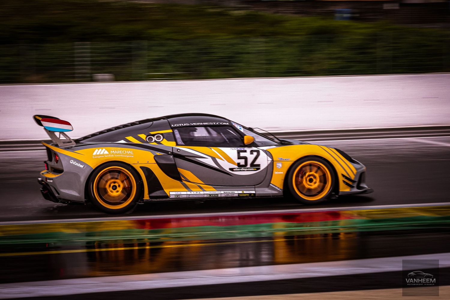 Yellow and gray race car number 52 speeding on a wet track during a motorsport competition.