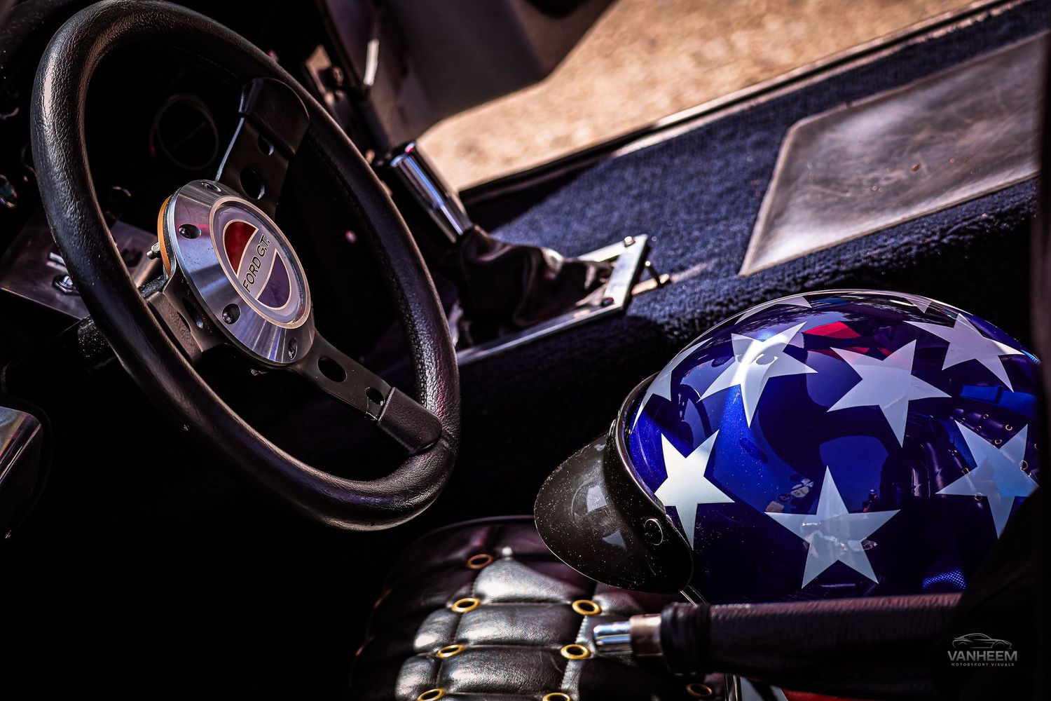 Interior view of a vintage car with a stars and stripes motorcycle helmet resting on the seat beside the steering wheel.
