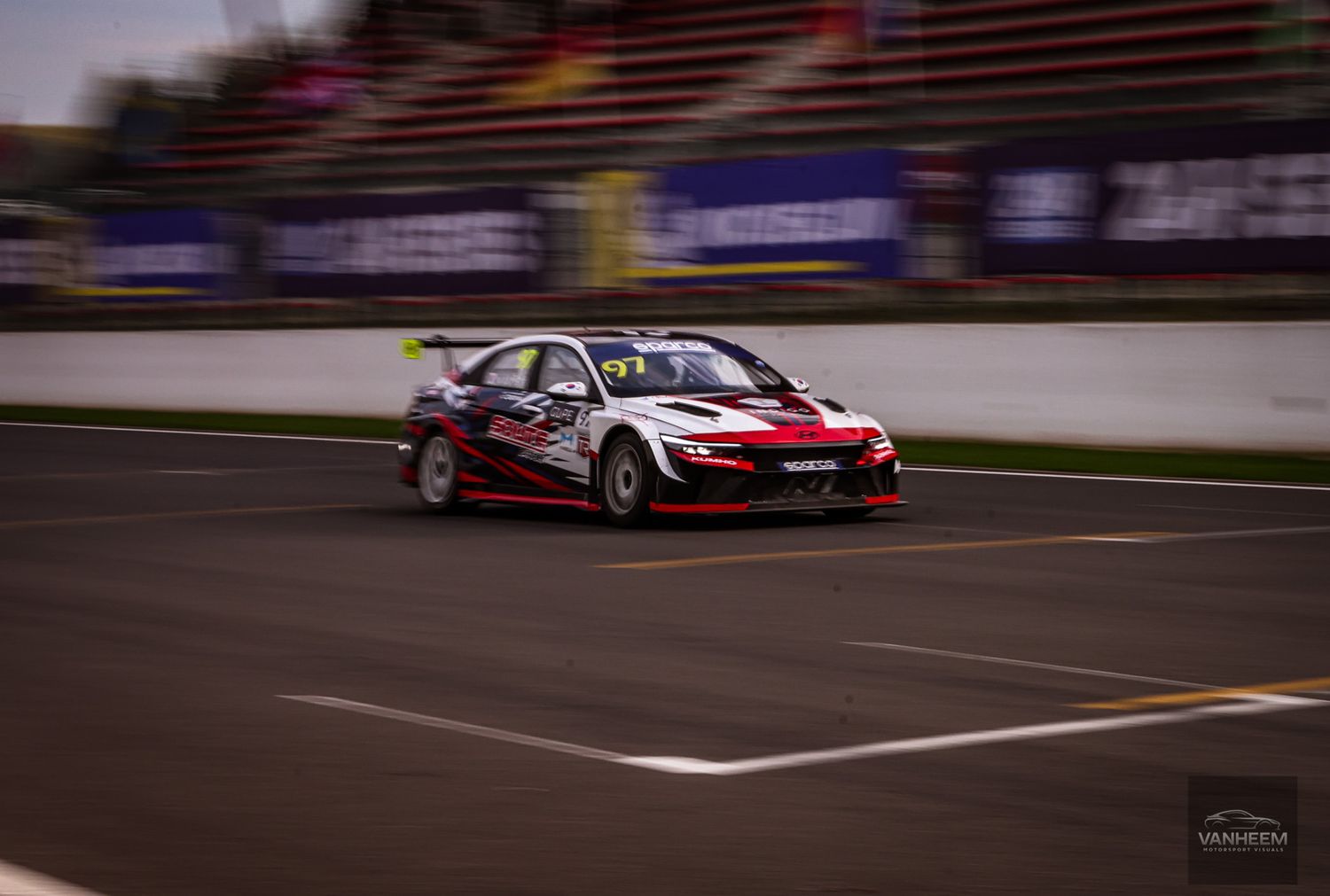 A red and white racing car speeding on a track during a competitive motorsport event.