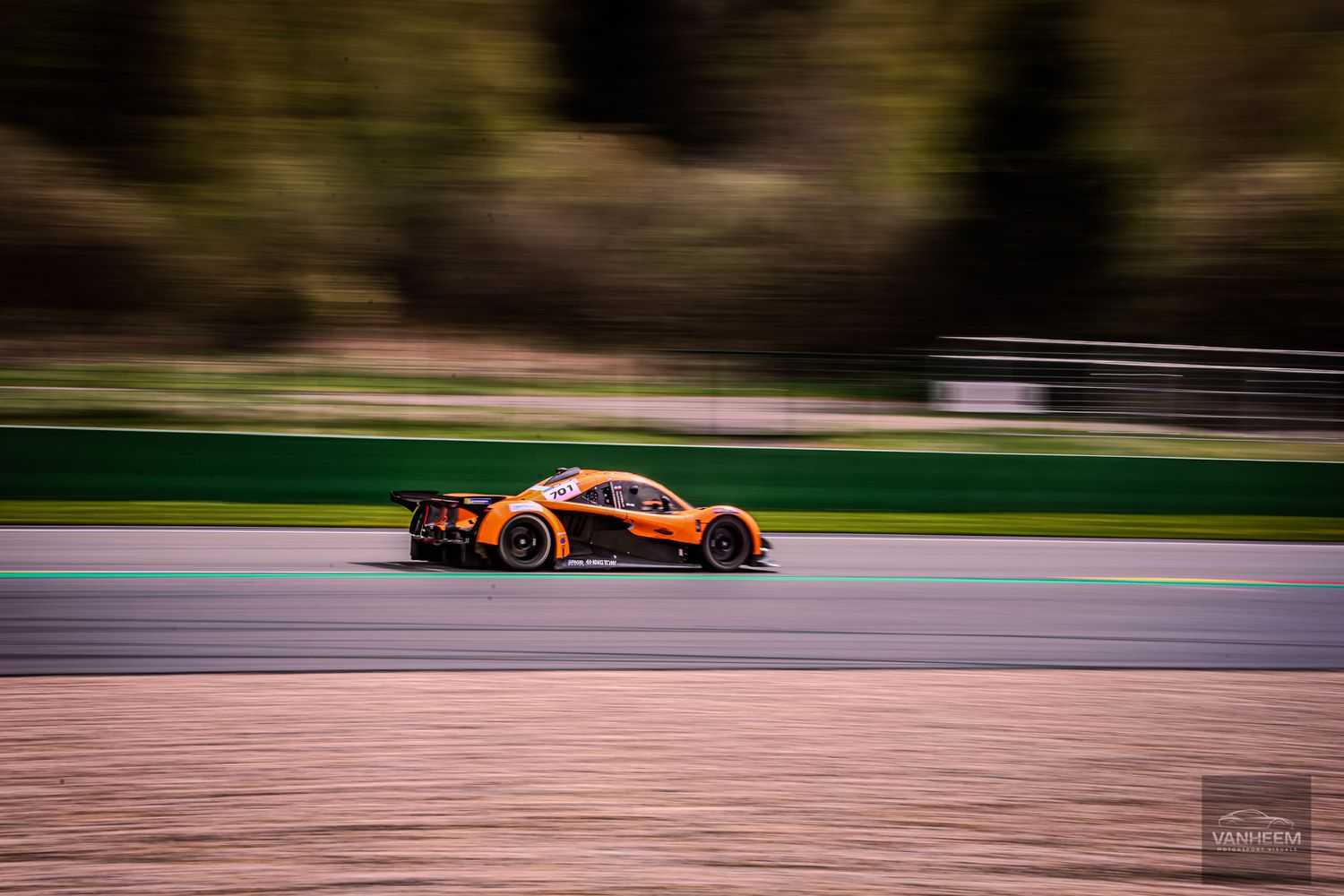 Orange McLaren GT3 race car speeding on track with motion blur background at racing circuit.