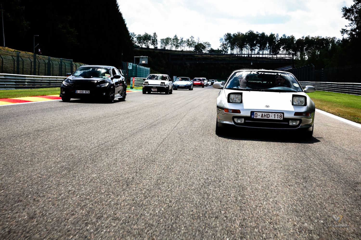 Classic sports cars racing on a circuit track during a motorsport event on a sunny day.