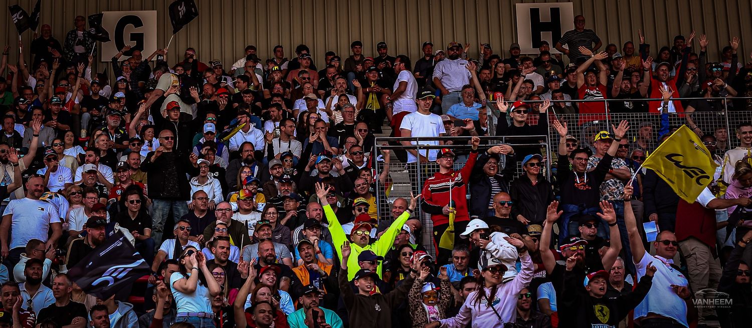 Large crowd of enthusiastic fans cheering in stadium stands during a daytime sporting event.