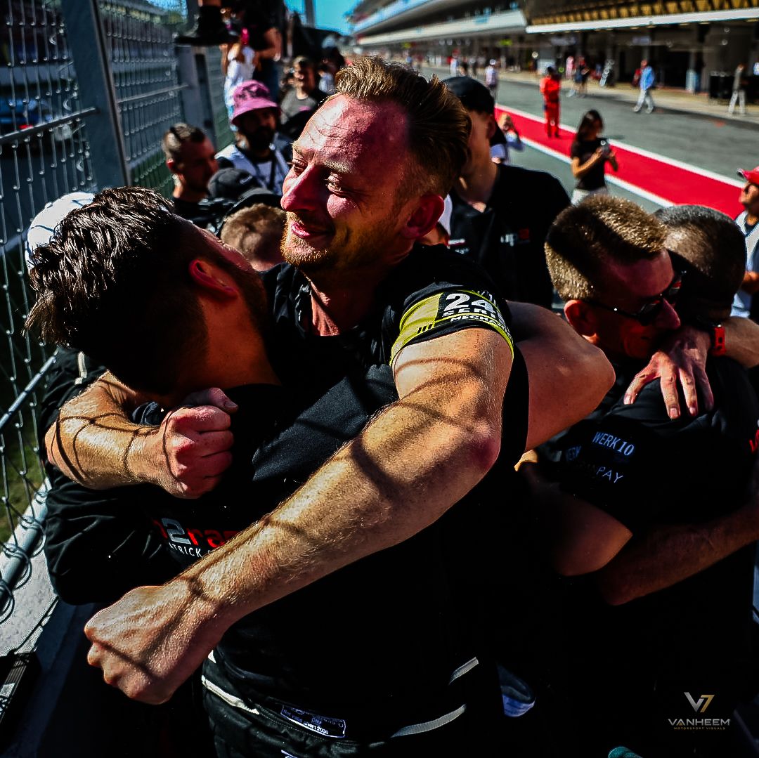 Racing team members celebrate with emotional embraces on the pit lane after a victory at a motorsport circuit.