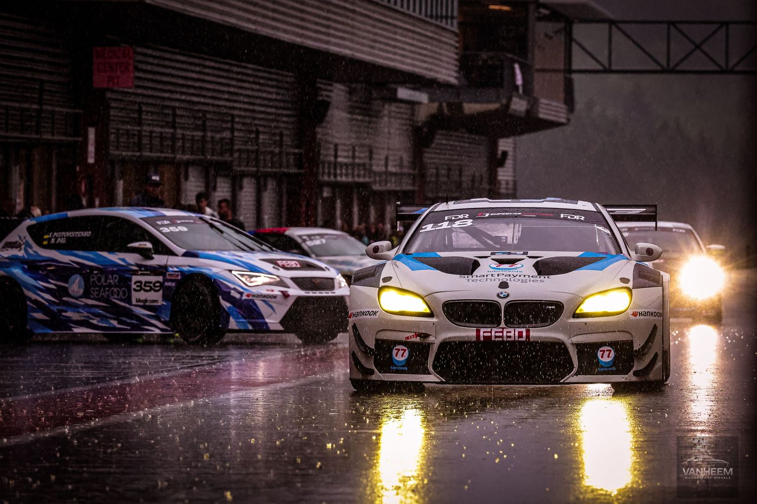 BMW M6 GT3 racing car leads a wet track lineup during a rainy motorsport endurance race event.