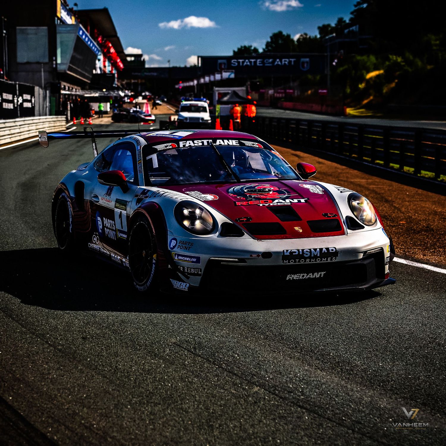 A Porsche 911 GT3 race car with Fast Lane livery navigates a circuit corner during a sunny motorsport event.