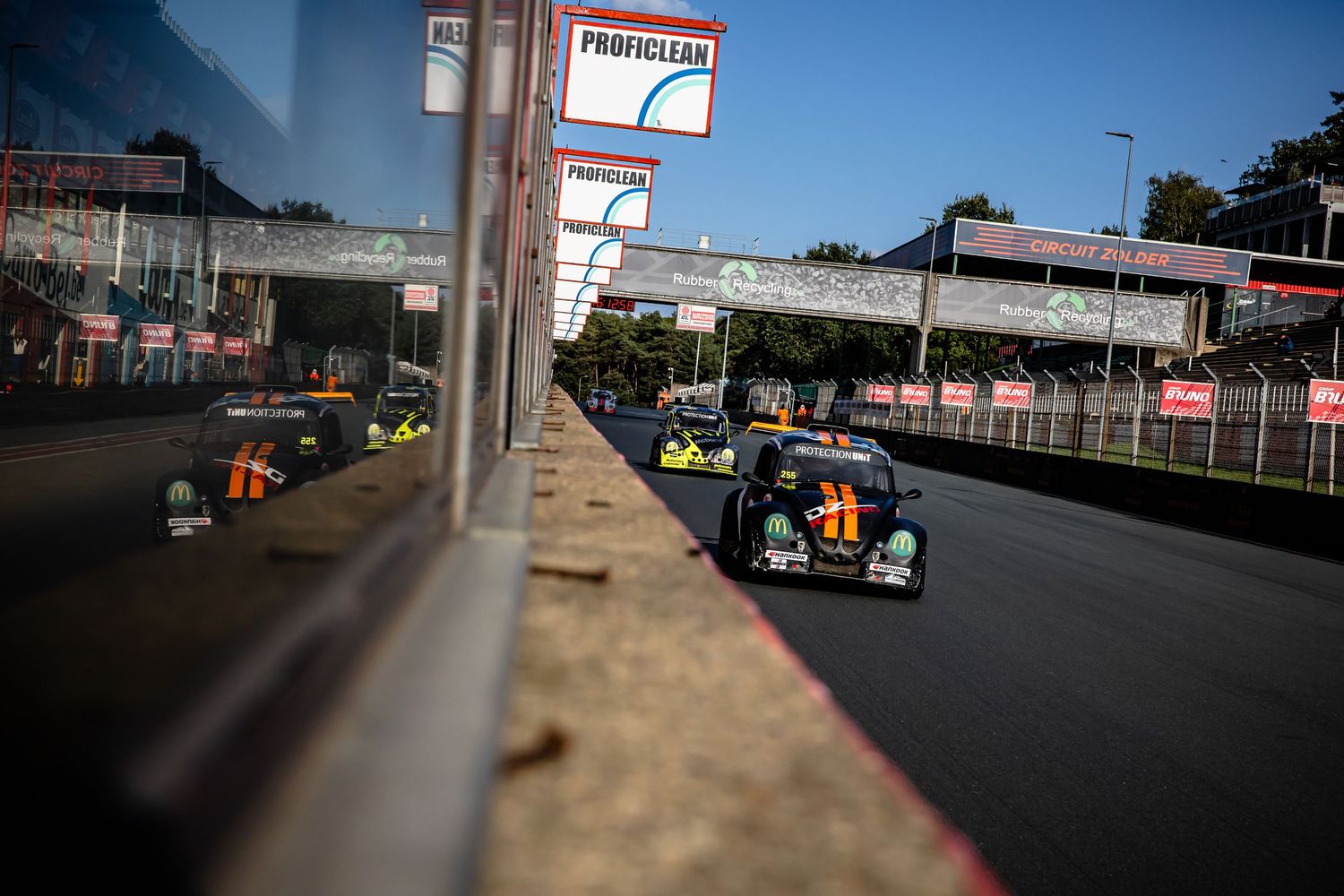 Racing cars compete on a street circuit track with barriers and grandstands visible in the background.
