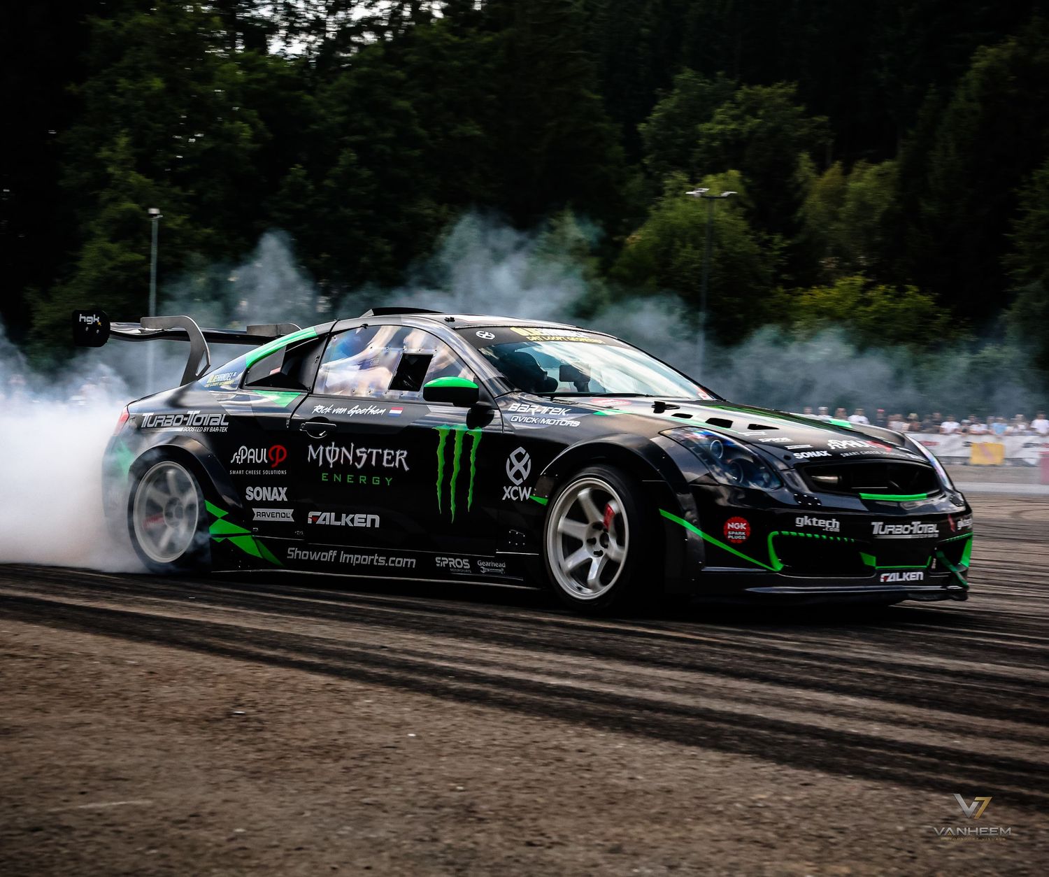Monster Energy drift car spinning tires with smoke on a race track surrounded by trees.