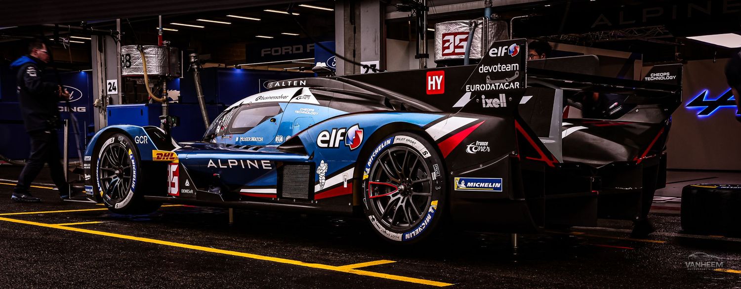 Alpine racing car number 5 in blue and white livery parked in a dark pit garage at a motorsport endurance race.