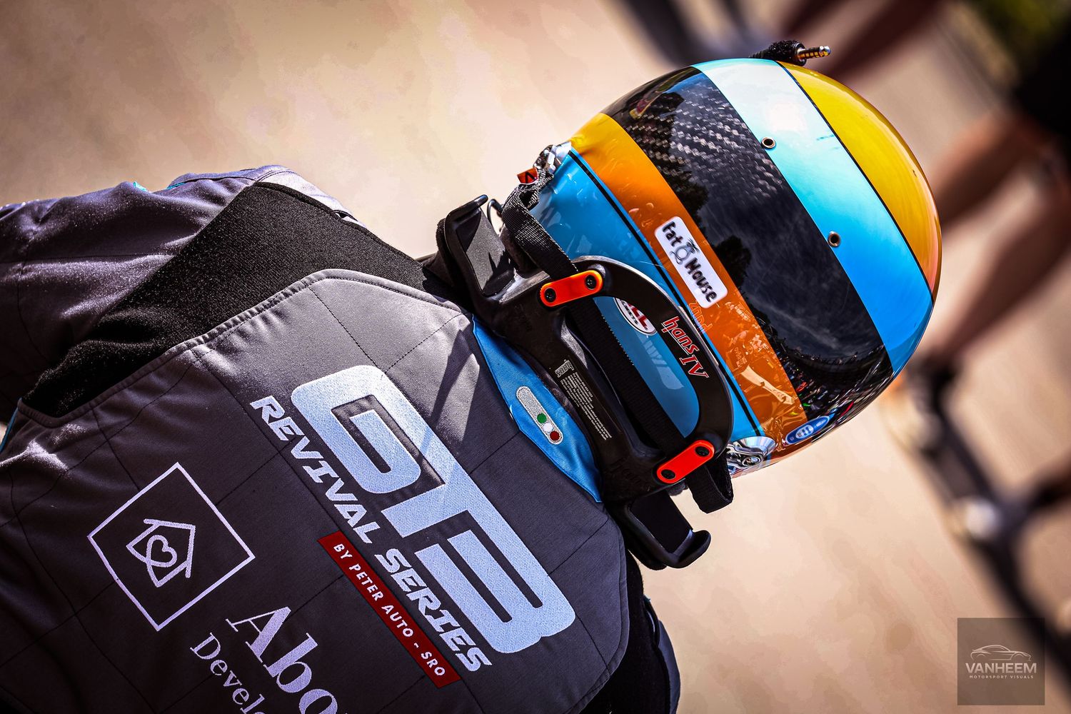Close-up of a racing driver wearing a colorful blue and orange helmet with GT Revival Series branding on their jacket.