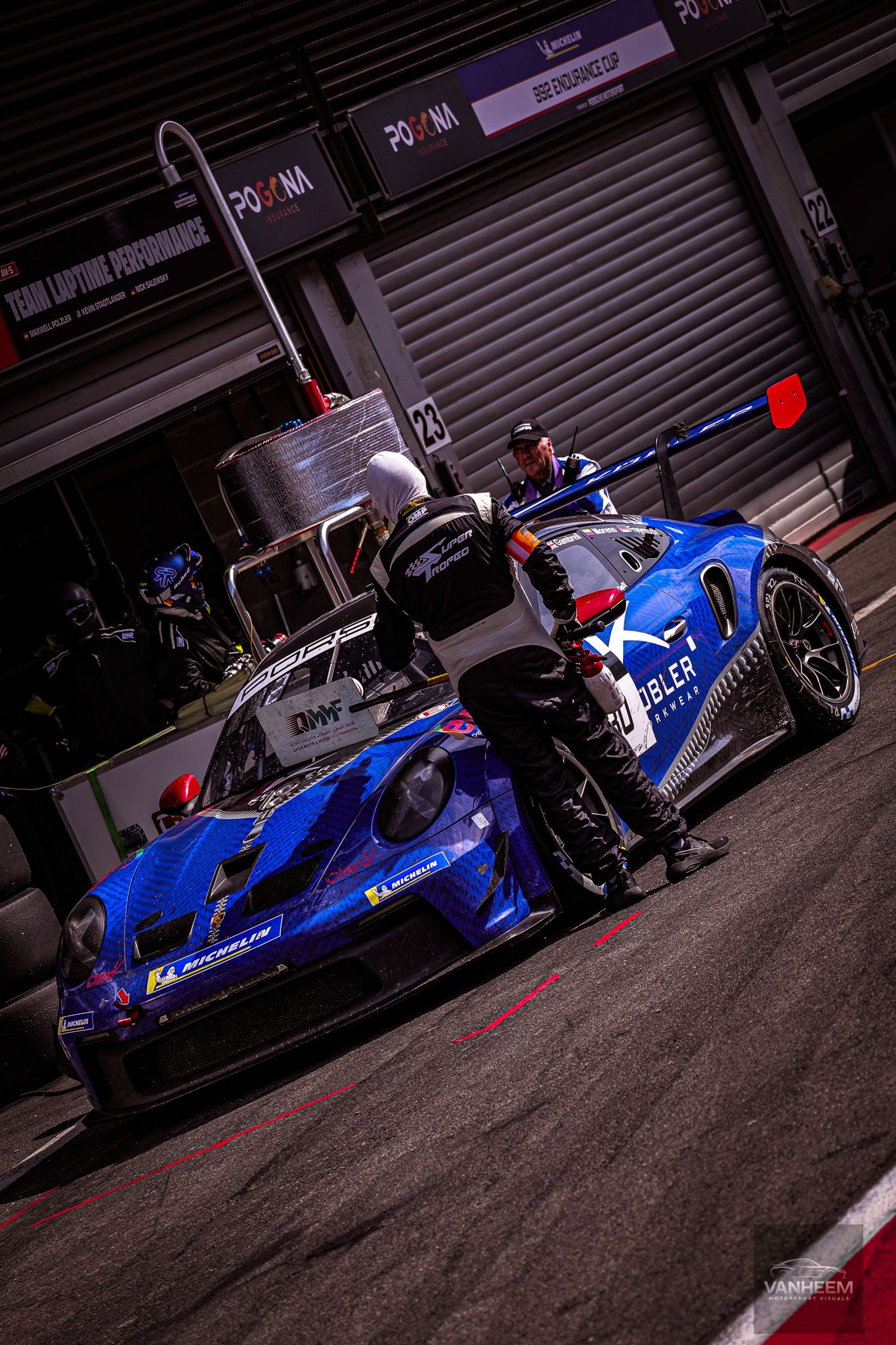 Blue racing cars lined up in pit lane with dramatic lighting and shadows.