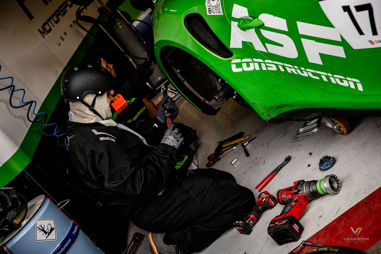 Mechanic working on green ASF Construction racing car number 17 in pit garage with power tools.