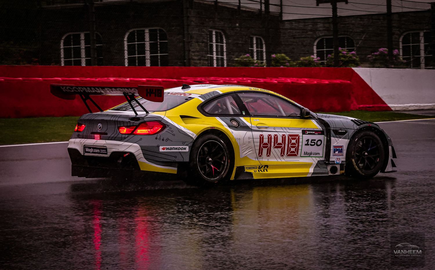 BMW M6 GT3 race car #48 in yellow and gray livery racing on wet track in rainy conditions.