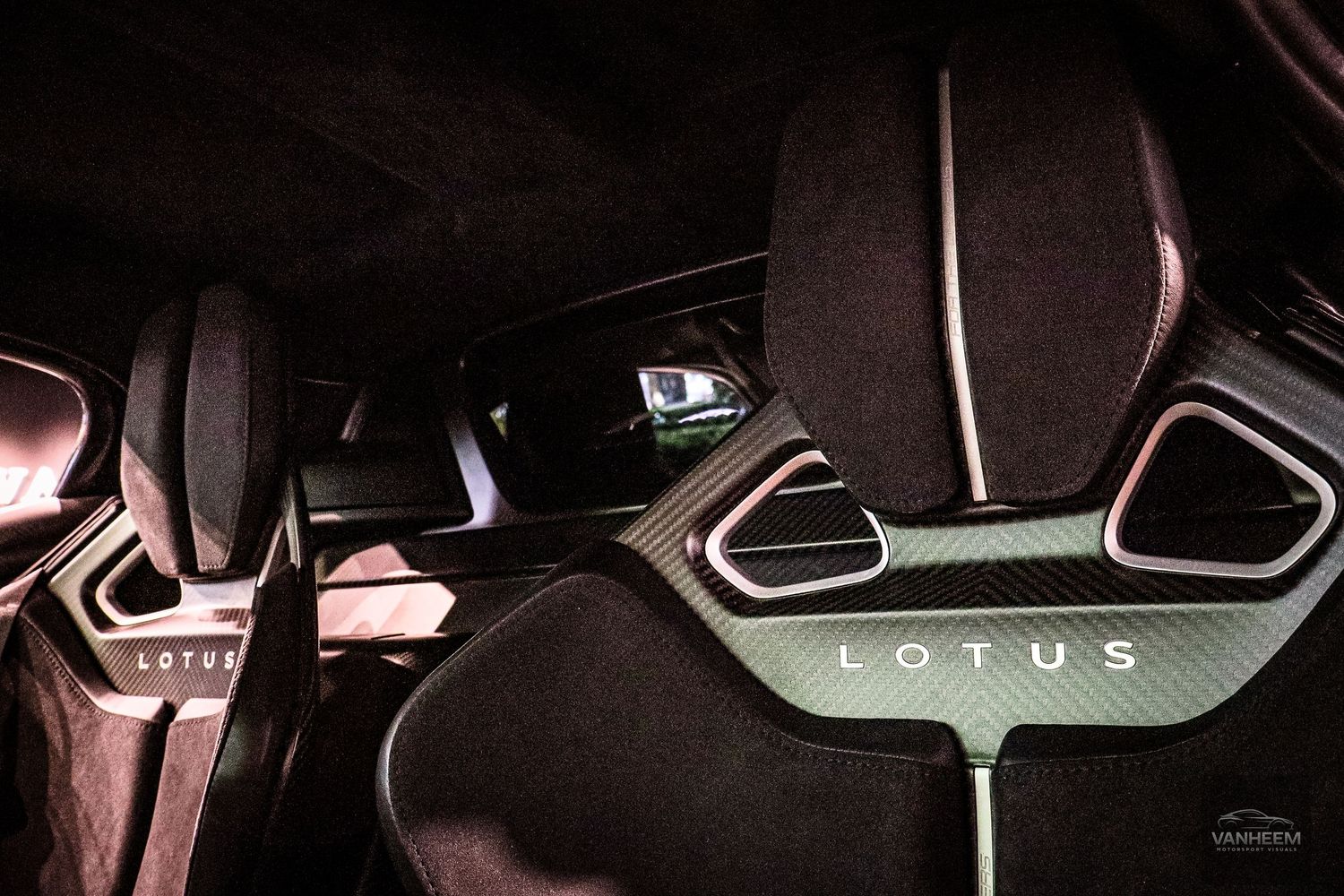 Lotus sports car interior featuring carbon fiber bucket seats with Lotus branding, illuminated in dramatic dark lighting.
